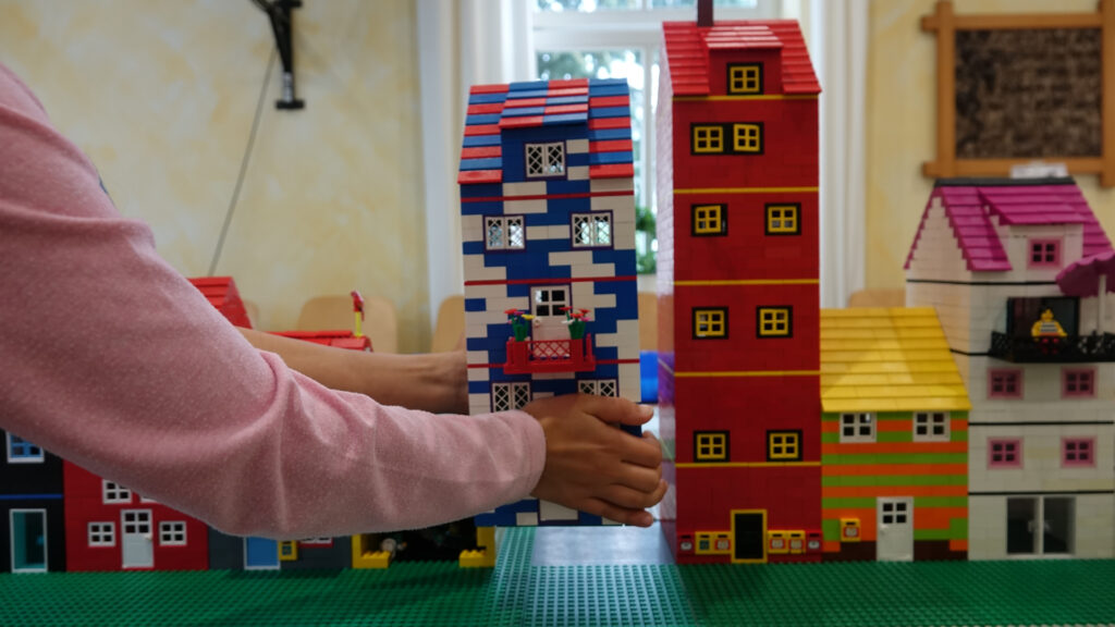 Eine Kinderhand setzt das selbstgebaute Haus in die Legostadt in der Christus-Gemeinde in Neukirchen-Vluyn