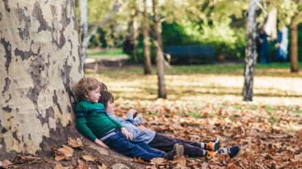 Zwei Kinder lehnen sich an einen großen Baumstamm