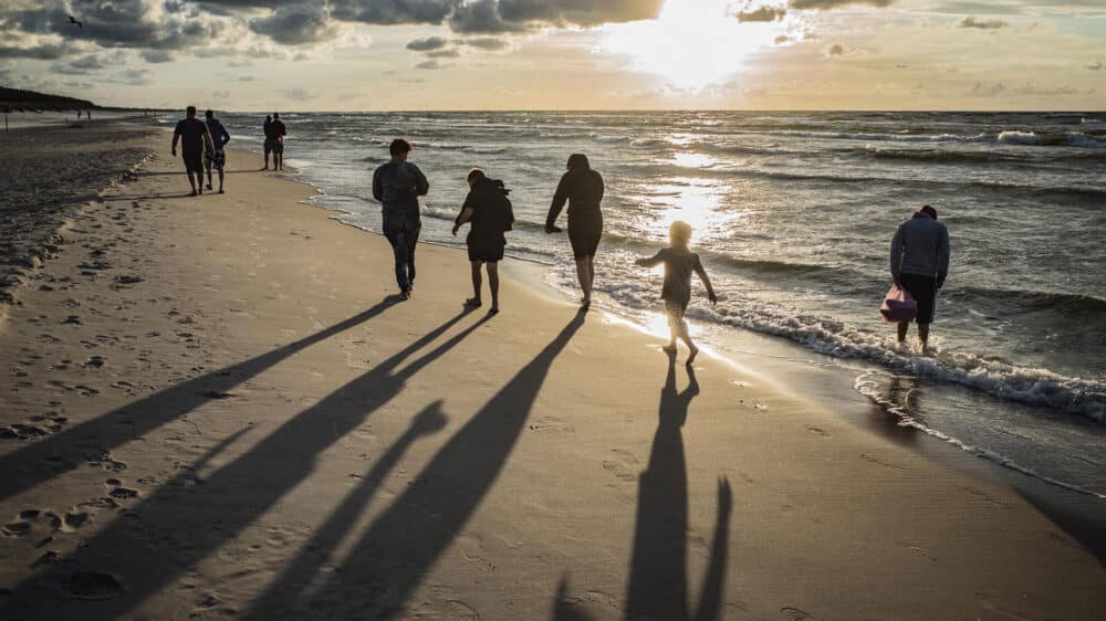 Kinder und Erwachsene spazieren am Strand entlang